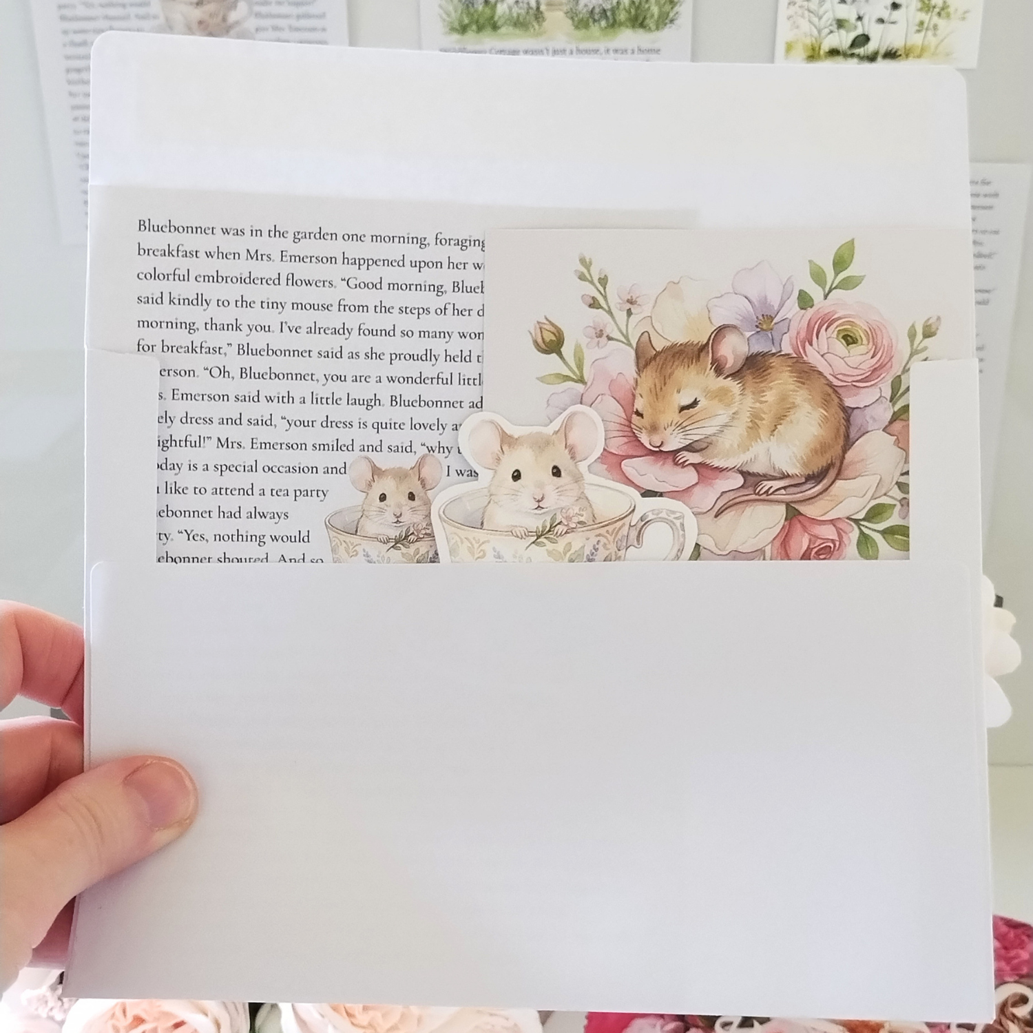 Hand holding a book with illustrations of mice and flowers on a white background