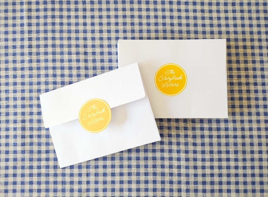 Two white envelopes with yellow circular stickers on a blue and white checkered fabric background